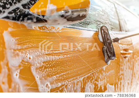 Side of car washed in self serve carwash, strokes from brush in white shampoo visible on yellow paint. Side of car washed in self serve carwash, strokes from brush in white shampoo visible on yellow paint. 78836368