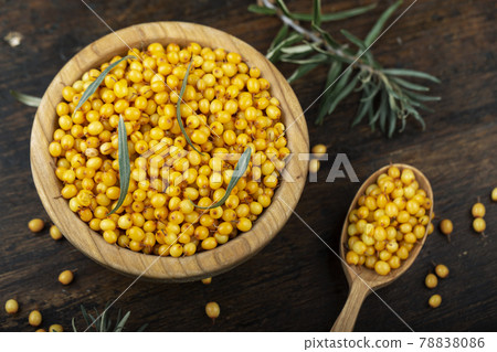 Sea buckthorn. Fresh ripe berry in wooden bowl and a spoon with leaves on wood background. 78838086