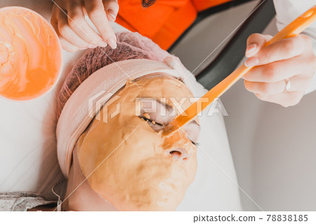 spa treatments in a beauty salon, hand of a professional beautician applying a gold mask on the client's face. spa treatments in a beauty salon, hand of a professional beautician applying a gold mask on the client's face. 78838185