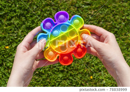 Hands press rubber pimples of pimpled anti stress pop it toy on green lawn Hands press rubber pimples of pimpled anti stress pop it toy on green lawn 78838999