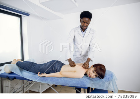 Male afro physiotherapist massaging a young woman's back at the medical office 78839089