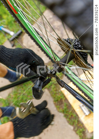 Bike mechanic man repairs bicycle in bicycle repair shop, outdoor. Hand of cyclist bicyclist examines, fixes modern cycle transmission system. Bike maintenance, sport shop concept. 78839214