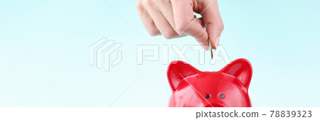 Womans hand throwing coin into red piggy bank closeup 78839323