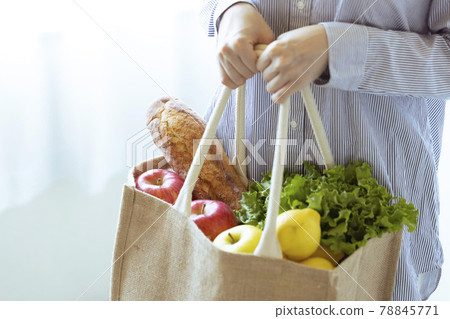 A woman holding vegetables and bread in an eco bag 78845771