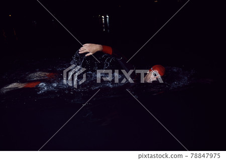 triathlon athlete swimming in dark night wearing wetsuit 78847975