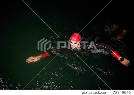triathlon athlete swimming in dark night wearing wetsuit 78849646