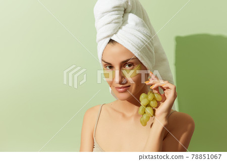 Woman using grapeseed-based eye patches on pastel green background. Natural sustainable skincare 78851067