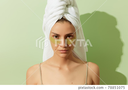 Woman in sunlight with eye patches on pastel green background. Morning skincare routine Woman in sunlight with eye patches on pastel green background. Morning skincare routine 78851075