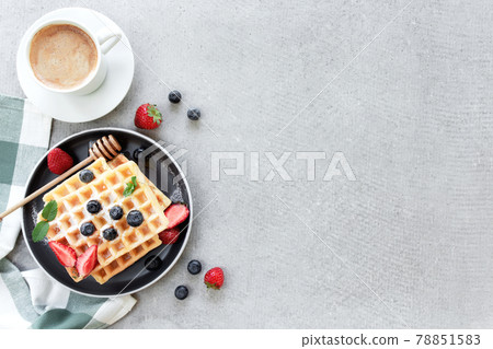 Waffles plate on table with blueberry, strawberry, mint and white cup of coffee Waffles plate on table with blueberry, strawberry, mint and white cup of coffee 78851583