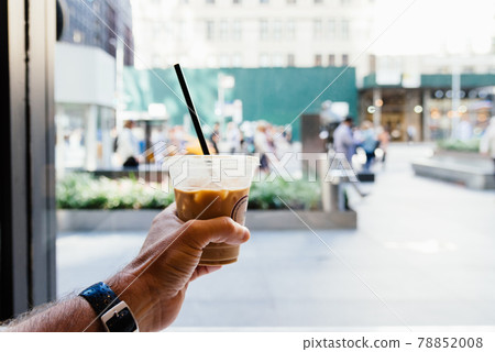 Man hand holding a plastic cup of iced coffee on urban background Man hand holding a plastic cup of iced coffee on urban background 78852008