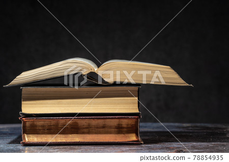 A stack of old books lying on a table on a dark background 78854935