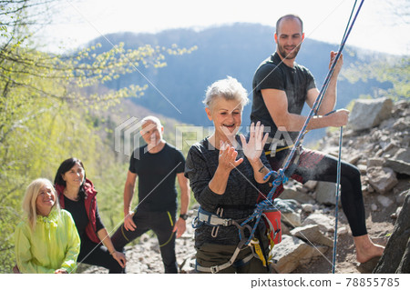 Group of seniors with instructor using chalk before climbing rocks outdoors in nature, active lifestyle. 78855785