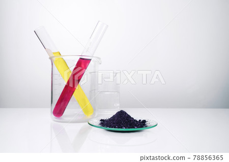 Cosmetic chemicals ingredient on white laboratory table. KMnO4 on chemical watch glass. Potassium Permanganate Liquid and Nickle chloride liquid in test tube in the background. 78856365
