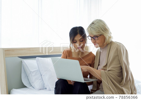 Asian daughter teach her adopted caucasian mother how to surf the Internet from a laptop computer. Happy mix skin family living together. Asian daughter teach her adopted caucasian mother how to surf the Internet from a laptop computer. Happy mix skin family living together. 78856366