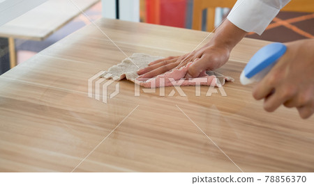 Closeup waiter's hand use a liquid cleaner and a towel to wipe off the stains on the table. 78856370
