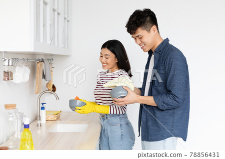 Asian guy helping his cheerful girlfriend washing dishes at kitchen 78856431