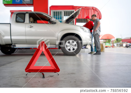 Red triangle reflector roadside warning on the floor. There is a broken pickup car in the background. 78856592