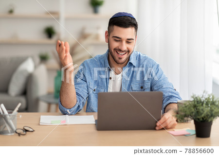 Smiling israeli man working on laptop computer at home Smiling israeli man working on laptop computer at home 78856600