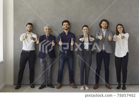 Business leaders showing thumbs up while standing against gray wall and looking at camera. 78857482