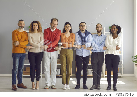 Diverse group of happy people standing in modern office, holding hands and smiling Diverse group of happy people standing in modern office, holding hands and smiling 78857510