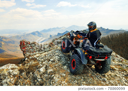 Man in helmet sitting on ATV quad bike in mountains 78860099