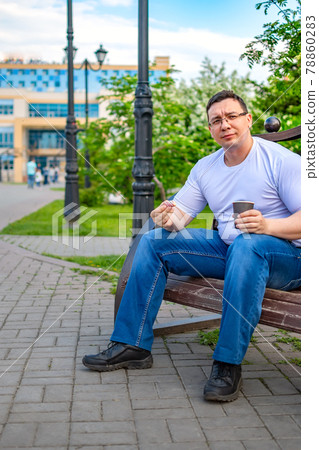 a man sits and eats a bun, in the park on a bench a man sits and eats a bun, in the park on a bench 78860283