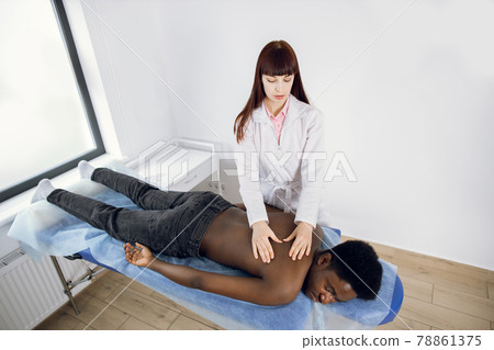 Caucasian woman rehabilitation specialist making treatment back massage for Afro-American man Caucasian woman rehabilitation specialist making treatment back massage for Afro-American man 78861375