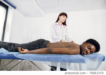 young woman physiotherapist make neck and shoulder massage for African American male patient 78861378