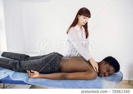 Professional female massage therapist making back massage for Afro-American male patient. Professional female massage therapist making back massage for Afro-American male patient. 78861380