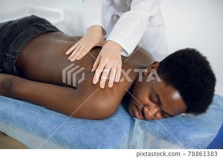 Close up of woman doctor physiotherapist manipulating shoulder blade on young African American man Close up of woman doctor physiotherapist manipulating shoulder blade on young African American man 78861383