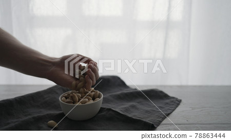 Man pick salted pistachios from white bowl on oak table 78863444
