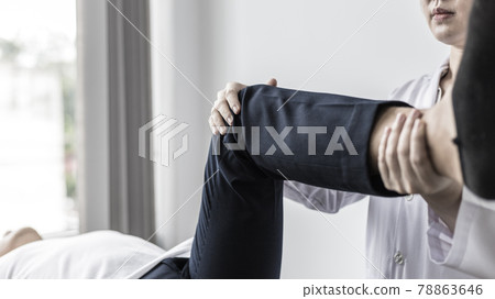 Physical therapy, Female physiotherapist treats legs and hips pain for a male patient attending in clinic, Bone arrangement, Non-surgical medical treatment, Modern medical techniques. 78863646