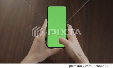 Man using phone with green screen on black wwalnut table 78863670