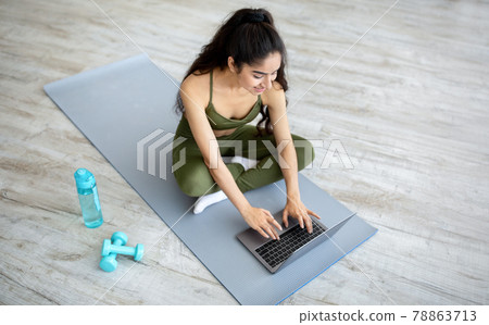 Millennial Indian woman watching online sports video on laptop before domestic workout, above view. Active lifestyle 78863713