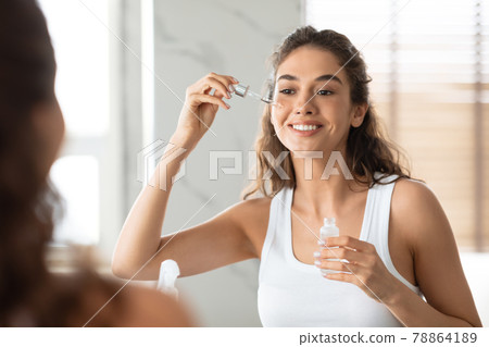 Attractive Female Applying Serum On Face Moisturizing Skin In Bathroom 78864189