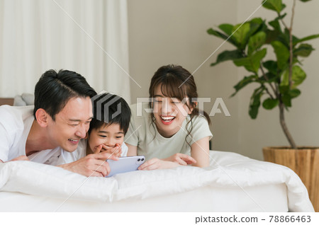 A family of three looking at a smartphone while lying on the bed in the bedroom A family of three looking at a smartphone while lying on the bed in the bedroom 78866463