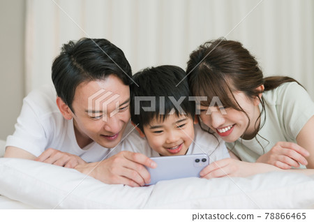 A family of three looking at a smartphone while lying on the bed in the bedroom A family of three looking at a smartphone while lying on the bed in the bedroom 78866465