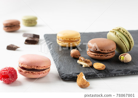 Variety of french macaroons with raspberry, nuts and chocolate on white wooden table. 78867801