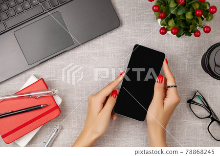 Woman with red manicure holding mobile phone on gray table 78868245
