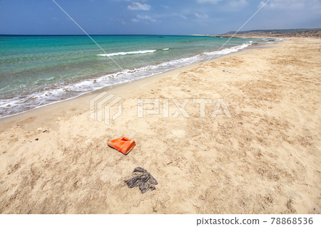 Beautiful wild beach with no tourists, crystal clear sea, but waste (plastic red bottle, black bag and other small debris) spoils the perfect picture. Ocean pollution concept. Beautiful wild beach with no tourists, crystal clear sea, but waste (plastic red bottle, black bag and other small debris) spoils the perfect picture. Ocean pollution concept. 78868536