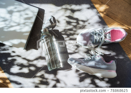 Laptop, sneakers and water bottle on a gray yoga mat background with direct sunlight and shadows. Online Fitness program, Home workout. Workout essentials. Top view, flat lay 78868625