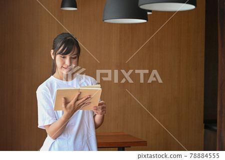 Smiling young female student reading book in library. Smiling young female student reading book in library. 78884555
