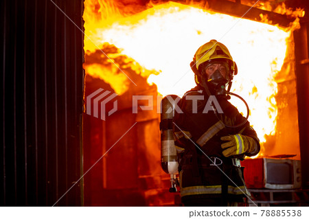 Fire on wall and ceiling in the kitchen behind firefighter man with protective and safety clothes Fire on wall and ceiling in the kitchen behind firefighter man with protective and safety clothes 78885538