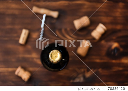 A dark bottle of wine next to blurry a corkscrew and a twisted cork on a wooden background. 78886420