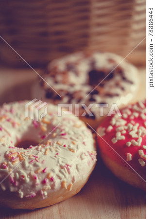 White, pink and brown glazed donuts on wooden background and near rattan basket . White, pink and brown glazed donuts on wooden background and near rattan basket . 78886443