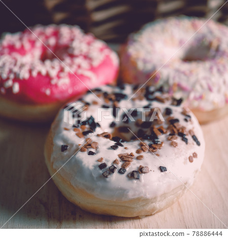 White, pink and brown glazed donuts on wooden background and near rattan basket . 78886444