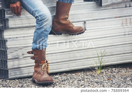 Men wear construction Boots safety footwear for worker at construction site. Engineer Wear Jeans Brown Boots Worker on Background of Refinery. Engineer safety industry fashion footwear walking outdoor Men wear construction Boots safety footwear for worker at construction site. Engineer Wear Jeans Brown Boots Worker on Background of Refinery. Engineer safety industry fashion footwear walking outdoor 78889364