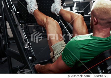 A man, a bodybuilder does exercises on his legs. The athlete trains his legs in the gym in the simulator. A man, a bodybuilder does exercises on his legs. The athlete trains his legs in the gym in the simulator. 78890970