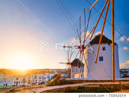 Famous tourist attraction of Mykonos, Greece. Traditional whitewashed windmills in row against sun. Summer, sunrise, travel destination, iconic view. Famous tourist attraction of Mykonos, Greece. Traditional whitewashed windmills in row against sun. Summer, sunrise, travel destination, iconic view. 78892654