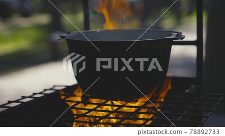 Cooking pot stands on a grate with a large flame of fire, cooking outdoors in a saucepan, outdoor tourist recipes, fiery dish on weekends, relaxing in the woods 78892733